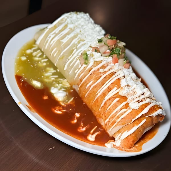 A large burrito covered in sour cream, pico de gallo, and red and green sauces on a white plate.