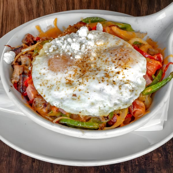 Mexican breakfast skillet with fried egg, cheese, peppers, onions, and meat on a wooden table.