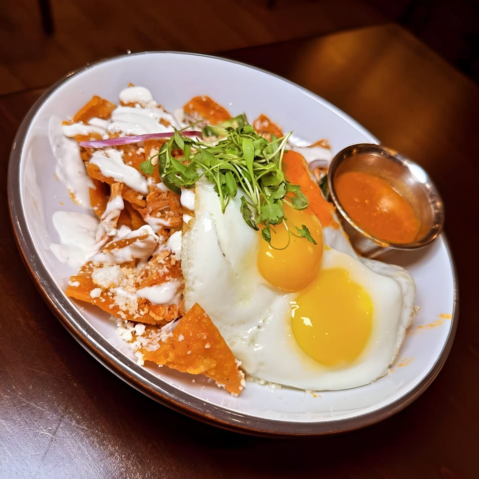 Chilaquiles with two fried eggs, crema, cheese, and microgreens, served with a side of salsa.