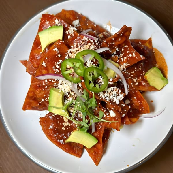 Chilaquiles with red sauce, crumbled cheese, avocado, jalapeños, red onion, and microgreens.