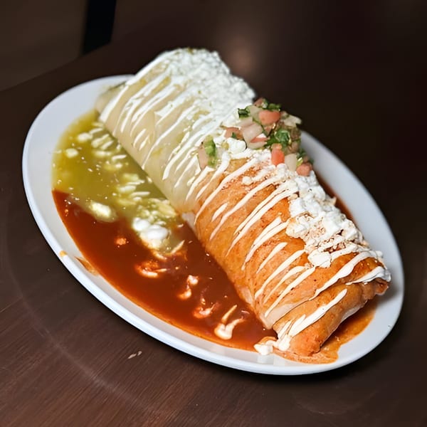 A large burrito covered in sour cream, pico de gallo, and red and green sauces.
