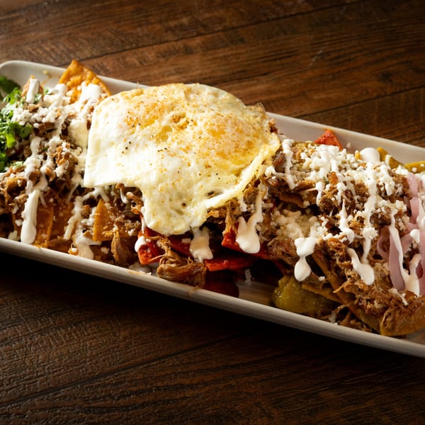 Chilaquiles with shredded pork, a fried egg, cheese, sour cream, and red onions on a white plate.