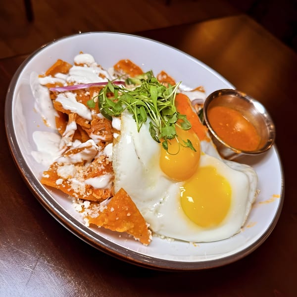 Chilaquiles with two fried eggs, crema, cheese, and microgreens, served with a side of salsa.