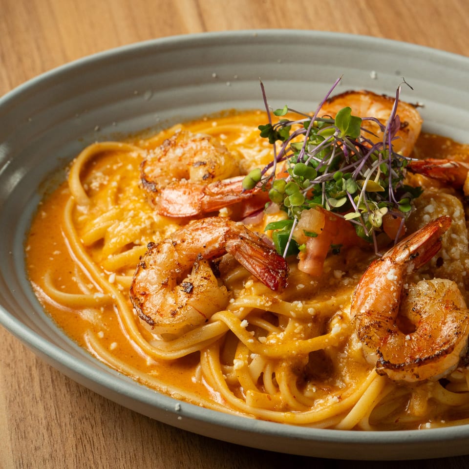 Shrimp linguine pasta in a creamy orange sauce, garnished with microgreens and parmesan cheese.